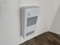 A white wall-mounted heater with a vent and a control knob in a minimalist interior design