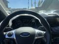 Steering wheel of a 2014 Ford Escape with Ford logo and various dashboard gauges visible in the background