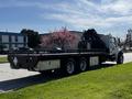 A 2012 Freightliner M2 112 truck with a flatbed and a mounted crane on the back positioned on a street