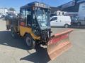 A yellow and black 2010 Trackless MT6 with a snow plow attachment in the front and a cab for the operator