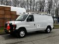 A white 2011 Ford Econoline van with an extended roof rack and traffic cones on the roof