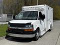 A white 2013 Chevrolet Express van with a sleek design and a flat front features chrome accents and a boxy cargo area with a rear door
