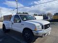 A 2000 Ford F-350 Super Duty pickup truck with a white exterior and black rims parked with a flatbed and a cardboard box in the back