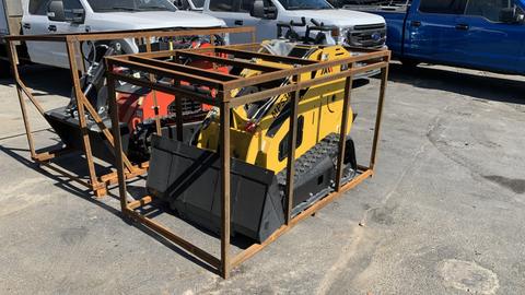 A yellow 2024 MachPro MP-S300 compact loader secured in a metal frame with a bucket attachment and tracks visible