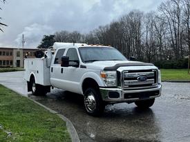 2014 Ford F-350 SD in white with a utility bed and orange lights on the roof parked on a wet surface