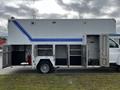 A 2006 GMC C5000 with a white exterior featuring blue stripes and several open storage compartments on the side