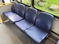 A row of four blue, upholstered seats in a bus with a textured surface and a sturdy metal frame