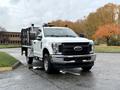 A 2019 Ford F-350 SD with a flatbed, featuring a white exterior, black grille, and mounted lights on the roof, parked on a paved surface