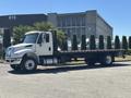 A white 2018 International DuraStar flatbed truck with a long bed and chrome accents parked on a lot