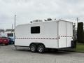 A white, two-axle trailer with red stripes and a small window on the side designed as a mobile office for shuttle operations