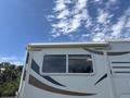 A 2018 Westland Travelaire with a large window and awning on the side displaying a sleek design with curved lines in tan and brown colors