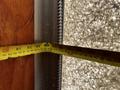 A yellow measuring tape is extended measuring a space between two surfaces, showing various measurements along the tape