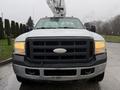 A 2006 Ford F-450 with a large front grille and orange lights on the roof facing forward with a bucket lift attached behind the cab