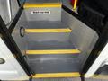 Metal stairs with yellow tread markings leading up into a bus interior featuring a "Watch Your Step" sign