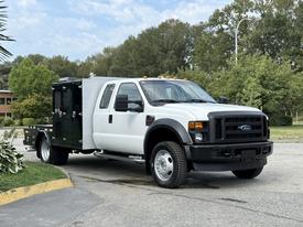 A white 2008 Ford F-450 SD pickup truck with a flatbed and black utility box attached on the side