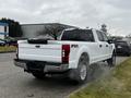 A white 2020 Ford F-350 Super Duty pickup truck with a crew cab and FX4 off-road package is emitting exhaust smoke from its rear