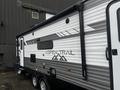 A 2022 Aspen Trail travel trailer with a sleek gray and white design featuring a door and windows on the side alongside the brand name and mountain logo graphics