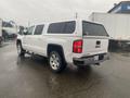 A white 2015 GMC Sierra 1500 parked with a truck cap on the bed showcasing its rear and side features