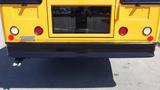 A yellow 2014 Freightliner Thomas Diesel bus viewed from the rear with round red brake lights and a silver exhaust pipe on the left