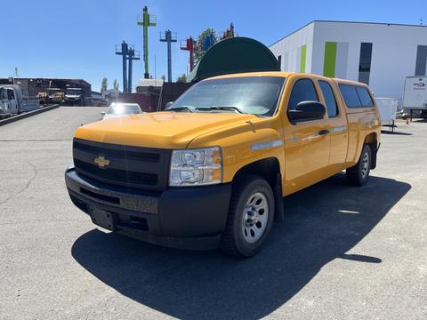 A yellow 2013 Chevrolet Silverado 1500 pickup truck with a cap on the bed is positioned at an angle, showcasing its front and side features