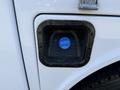 A blue fuel cap is secured within a black rim on the side of a white vehicle