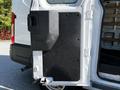 A 2023 Ford Transit van with an open side door featuring a black panel and interior shelves visible inside the vehicle