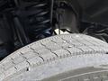 A close-up view of a treaded tire with visible wear patterns from a 2016 Ford F-550 showing part of the suspension system in the background