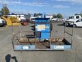 A 1997 Genie S-65 4X4 aerial lift with a blue platform and a metal safety railing at the front facing forward