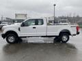 A white 2017 Ford F-250 Super Duty pickup truck with a flatbed and four-wheel drive parked on a wet surface