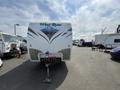 A rear view of a 2013 Wind River travel trailer featuring a mountainscape graphic and a sturdy hitch setup
