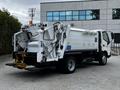 A 2014 Hino 195 garbage truck with a compacting mechanism and rear loading functionality parked at a commercial building