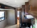 Interior view of a 2016 Jayco 265RLSW travel trailer featuring a kitchen area with stove and cabinets along with a bathroom door and bedroom visible in the background