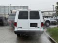 A white 2013 Ford E-350 van seen from the rear with no license plate and fog or steam rising from the exhaust