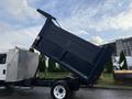 A 2015 Isuzu NPR HD truck with a raised dump bed positioned at an angle