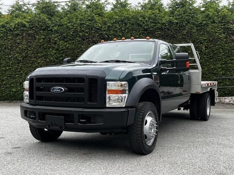 A 2008 Ford F-550 truck in dark green with a flatbed and chrome accents, featuring a robust front grille and a tall frame, positioned in a three-quarter view