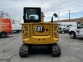 A yellow 2024 Caterpillar 306 excavator viewed from the rear with its tracks visible and the CAT logo prominently displayed on the back