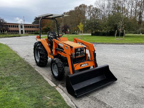 A 2001 Agco ST40 tractor with an orange body and black front loader bucket, featuring a simple dashboard and steering wheel, parked on a gravel surface.