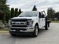 2019 Ford F-350 SD with a chrome front grille and a black hood parked on a driveway with a flatbed attached in the rear