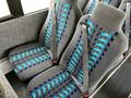 Two gray bus seats with blue and black patterned upholstery, equipped with seat belts, are positioned side by side in the foreground