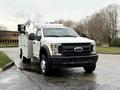 A white 2017 Ford F-550 truck with a utility bed and a raised aerial work platform on the roof
