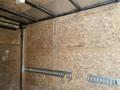 A 2020 Stealth Enterprises Trailer interior showing wooden walls with metal tracks for securing cargo and two yellow straps attached to the tracks