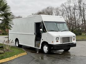 A 2018 Ford E-450 delivery truck with a white exterior and a boxy design, featuring an open driver's side door and a black front grille