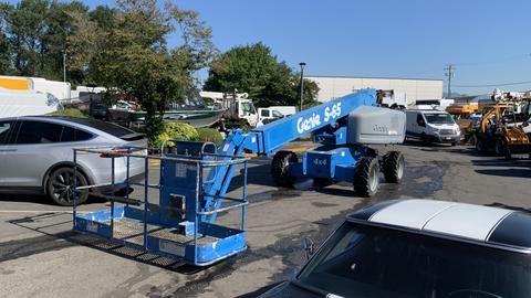 A blue 2008 Genie S-65 Boom Lift with a platform extended forward and a metal safety railing around the base