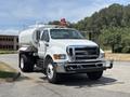 White 2015 Ford F-750 truck with a large tank attached to the rear and a red light on the roof parked on a paved area