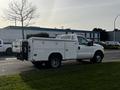 A white 2016 Ford F-350 SD truck with a utility body and open tool storage compartments on the sides