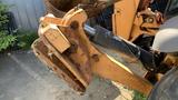 A 2015 Case 580 backhoe loader with a rusted bucket attachment and hydraulic arm in the foreground