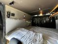 Interior view of a converted 2017 Mercedes-Benz Sprinter featuring a bed with bedding and shelves above
