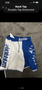 Blue and white MMA shorts with the word Warrior displayed prominently on the waistband and side, featuring a graphic design of skulls and flames on the blue side