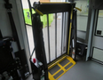 A yellow and black wheelchair lift with a mesh panel and control buttons positioned on the floor of a vehicle