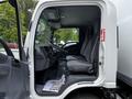 The image shows the driver's side of a 2018 Isuzu NPR truck with an open door revealing a spacious cabin featuring grey seats and a dashboard